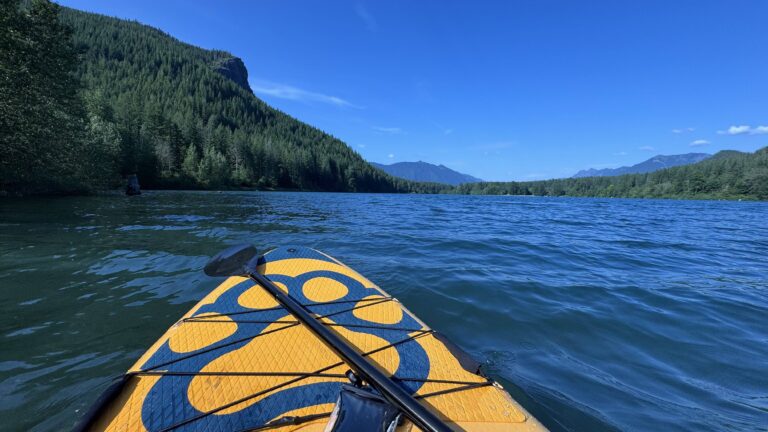 Kayaking on a calm lake surrounded by forested mountains in Washington State, viewed from the front of a kayak.