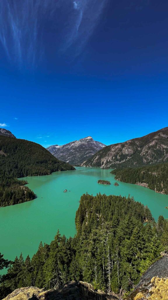 Turquoise waters of Diablo Lake surrounded by forested islands and mountain peaks in the North Cascades on a clear day.