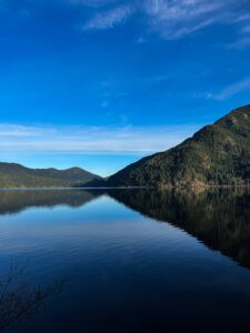 Clear blue sky reflected on the calm waters of Lake Crescent, surrounded by forested mountains in Olympic National Park.