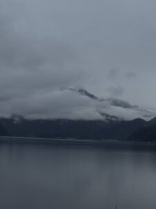 Misty clouds rolling over the mountains at Lake Crescent in Olympic National Park, with calm dark water and an overcast sky.