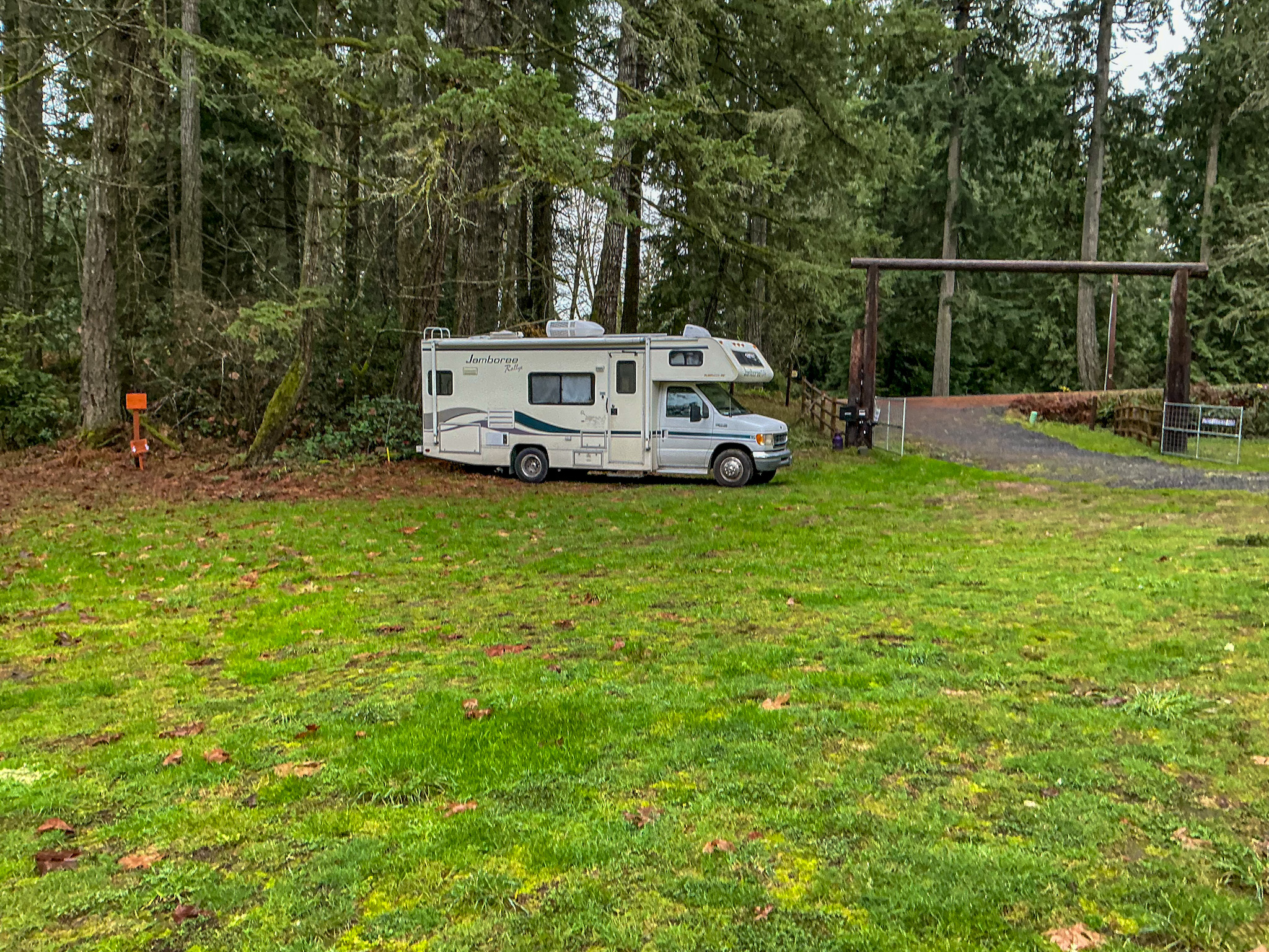 Class C RV parked on a grassy clearing surrounded by tall evergreen trees in Washington State.