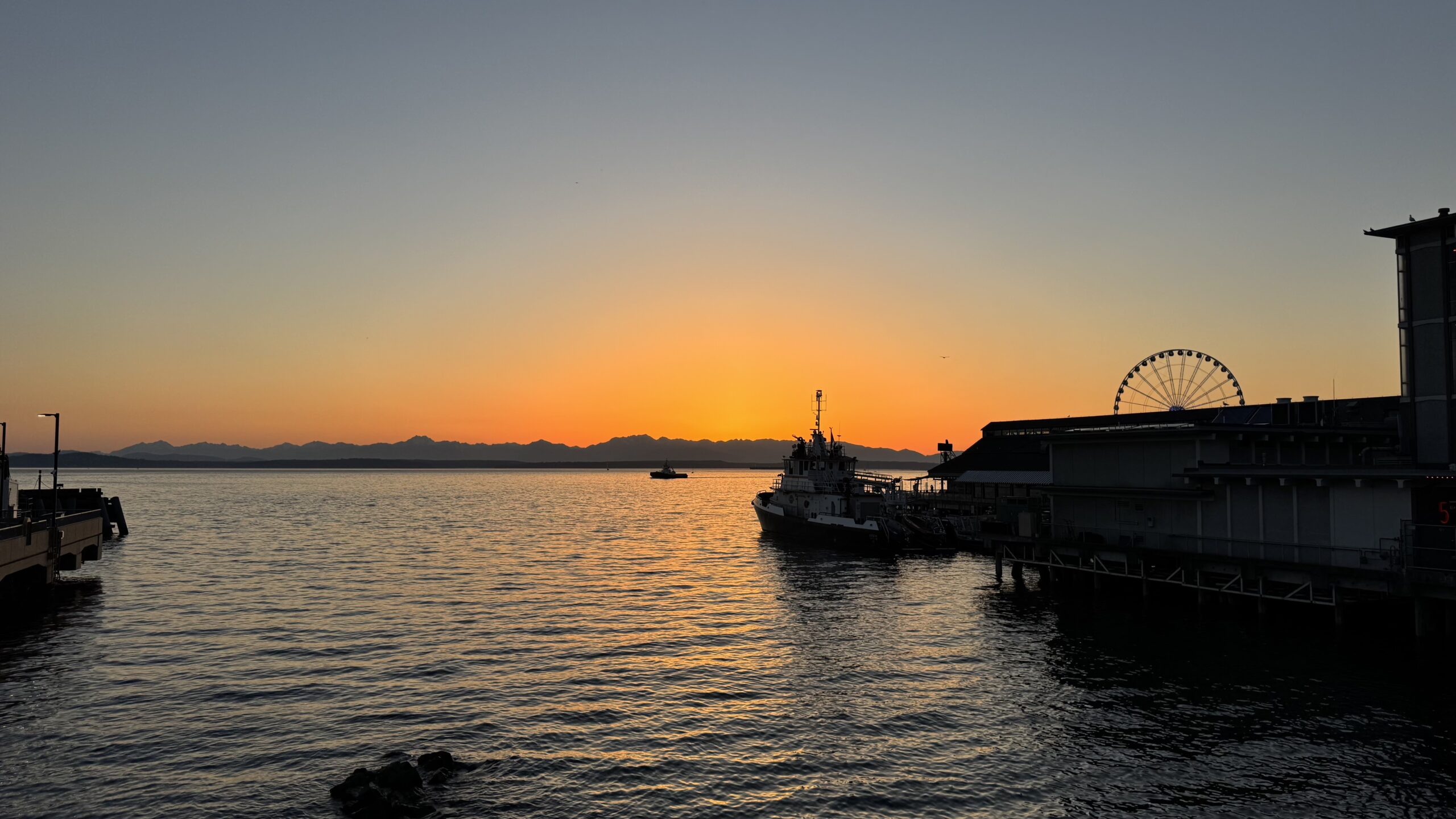 Sunset over Seattle waterfront with boats and the Seattle Great Wheel silhouetted against the orange sky.
