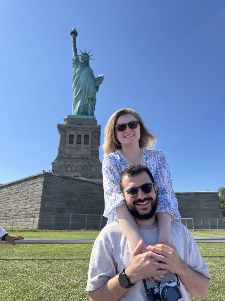 Couple posing in front of the Statue of Liberty in New York City.