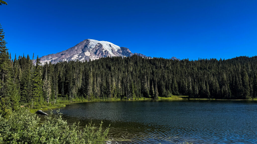Mount Rainier towering above an alpine lake surrounded by evergreen forest in Mount Rainier National Park.