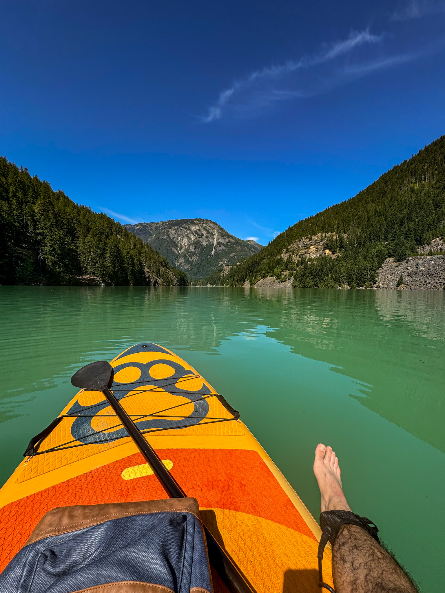 Person paddleboarding on turquoise Diablo Lake surrounded by forested mountains in North Cascades National Park, Washington.