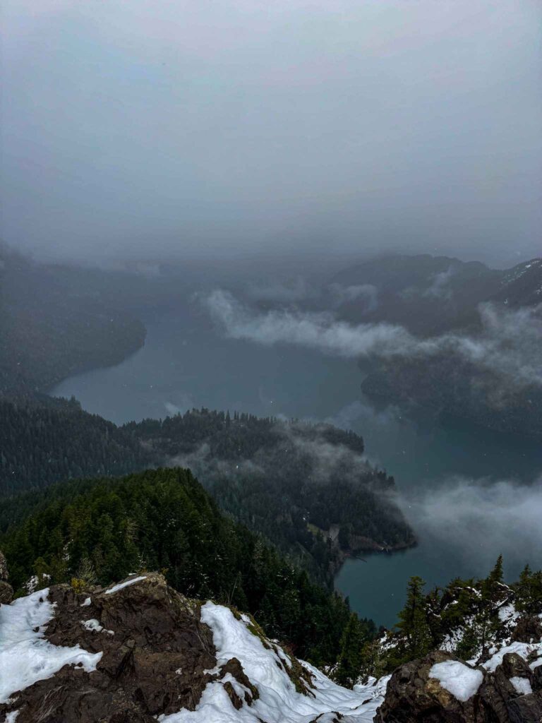 View of Lake Crescent from the Storm King Trail with misty clouds, forested islands, and snow-covered rocks in Olympic National Park.