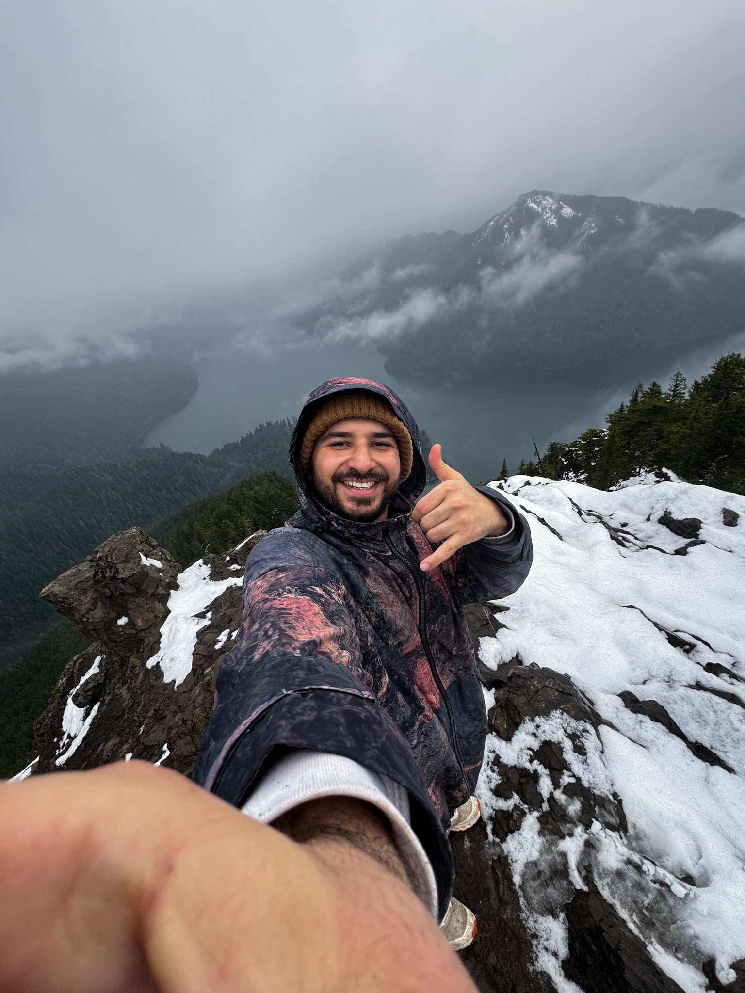 View from the Mount Storm King Trail overlooking Lake Crescent with misty clouds and snow-covered rock in Olympic National Park.
