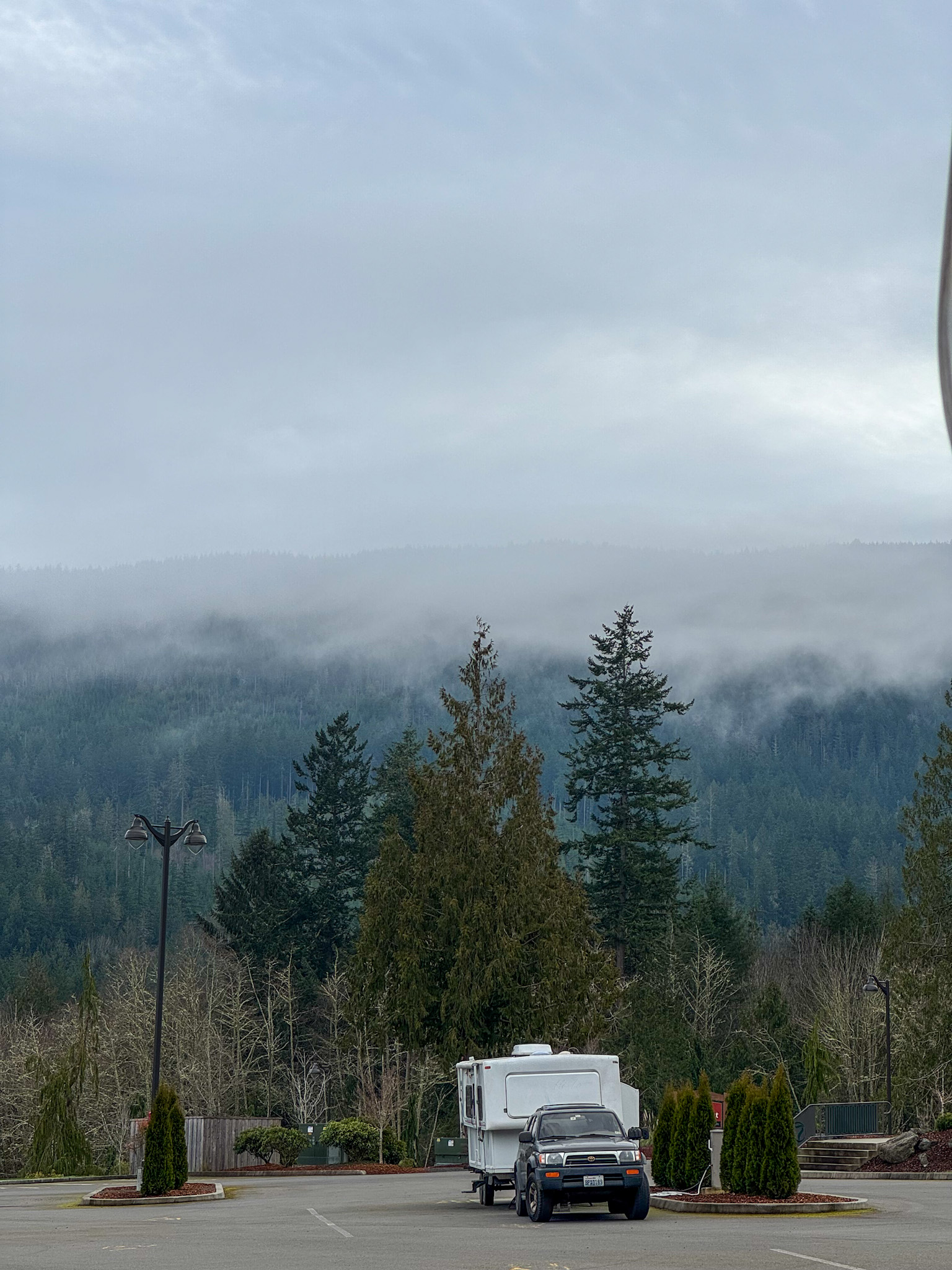 RV parked at 7 Cedars Casino RV parking area with misty forested hills in the background in Washington State.
