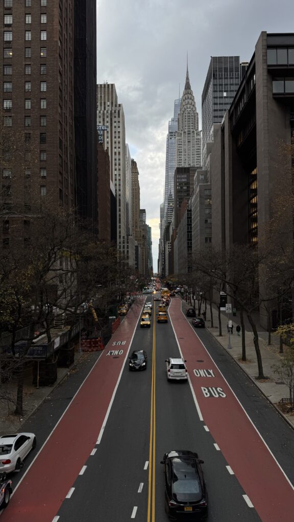View of the Chrysler Building along a busy Midtown Manhattan street with yellow taxis and bus lanes in New York City.
