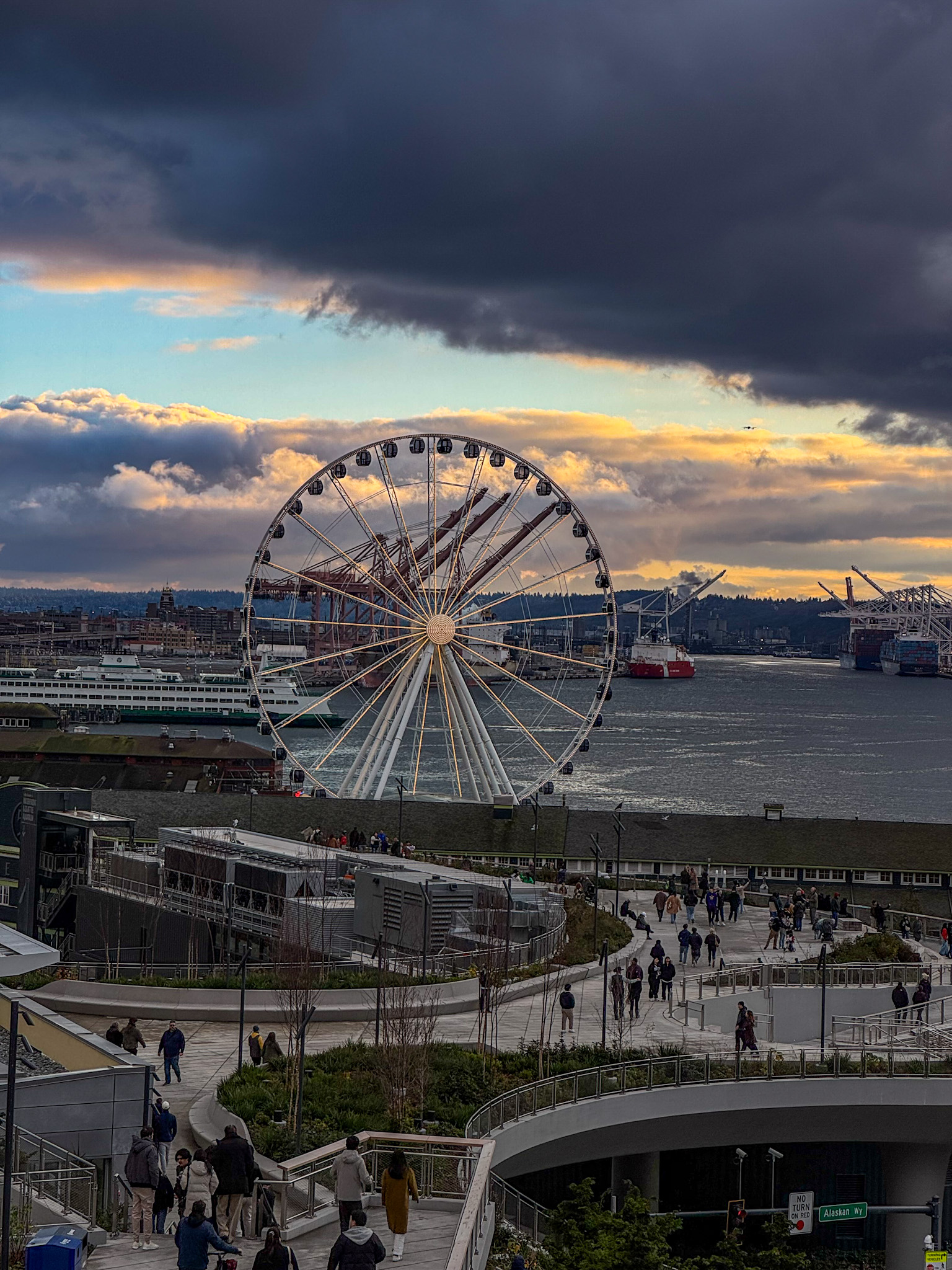 Seattle Great Wheel overlooking Elliott Bay with dramatic clouds and waterfront promenade.
