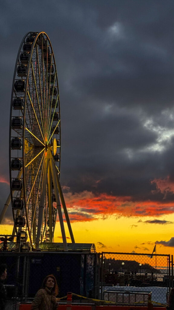 Seattle Great Wheel illuminated at sunset with dramatic clouds over Elliott Bay.