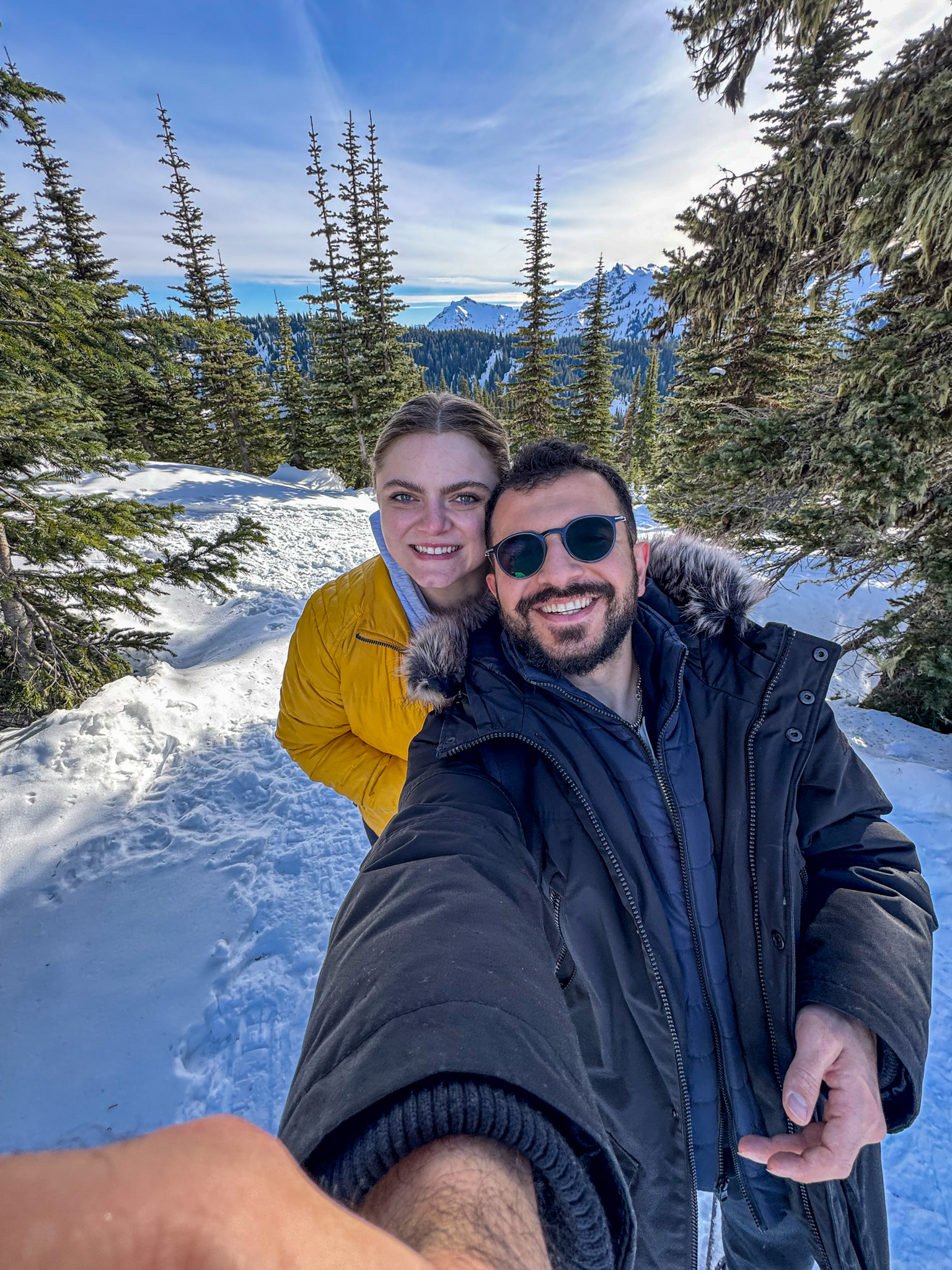 Couple taking a selfie in a snowy mountain landscape surrounded by evergreen trees in Washington State.
