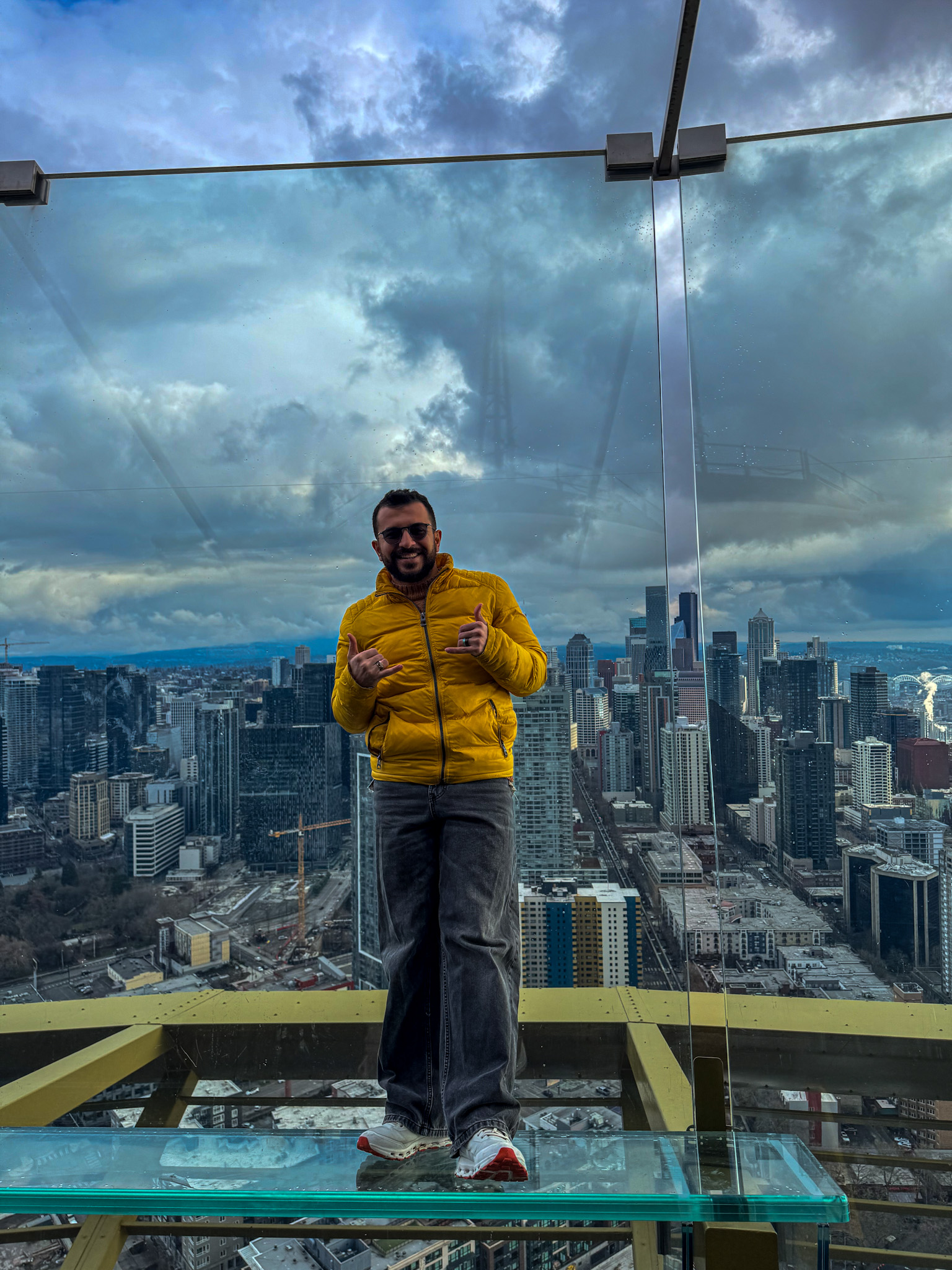 Person standing on the glass floor at the Space Needle observation deck with Seattle skyline in the background.
