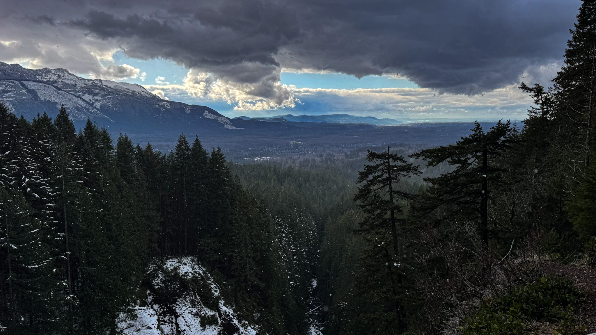 Snow-dusted evergreen forest and mountain valley under dramatic clouds in Washington State.