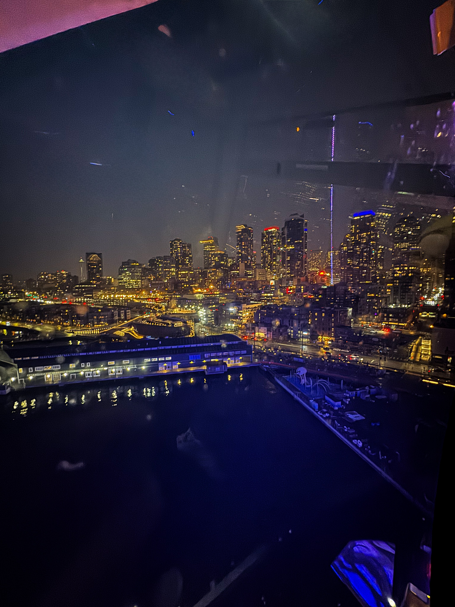 Seattle skyline at night with illuminated skyscrapers and waterfront reflections.
