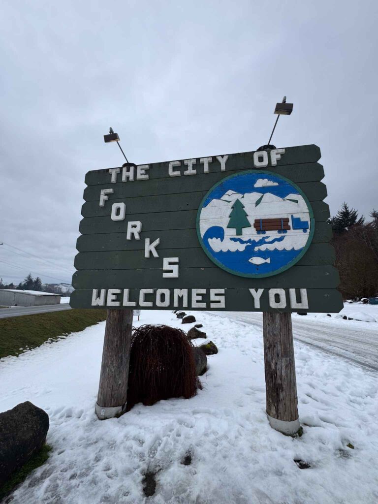 The City of Forks welcomes you sign standing beside a snowy road in Forks, Washington.