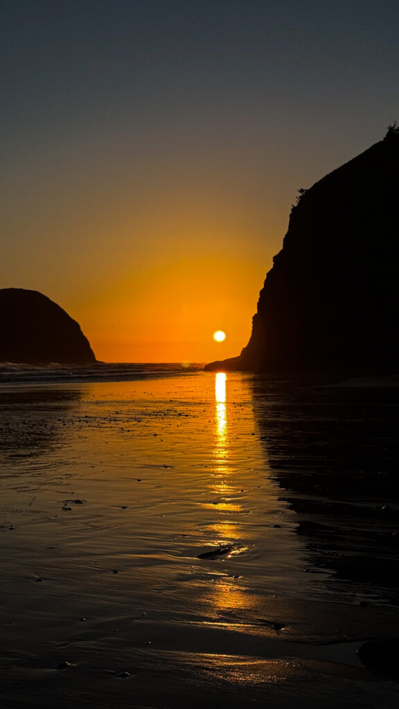 Sunset over Tunnel Beach on the Oregon Coast with sea stacks silhouetted against the orange sky.
