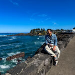 Traveler sitting on a coastal viewpoint overlooking the Pacific Ocean along the Oregon Coast.