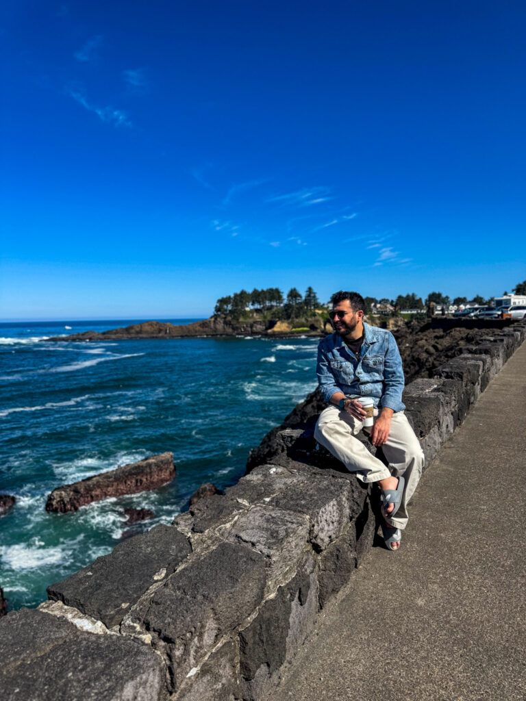Traveler sitting on a coastal viewpoint overlooking the Pacific Ocean along the Oregon Coast.