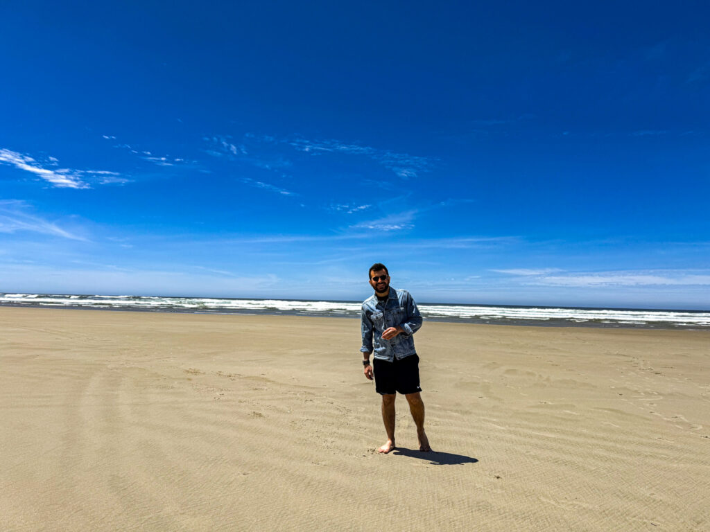 Person standing on a wide sandy beach along the Oregon Coast with the Pacific Ocean in the background.