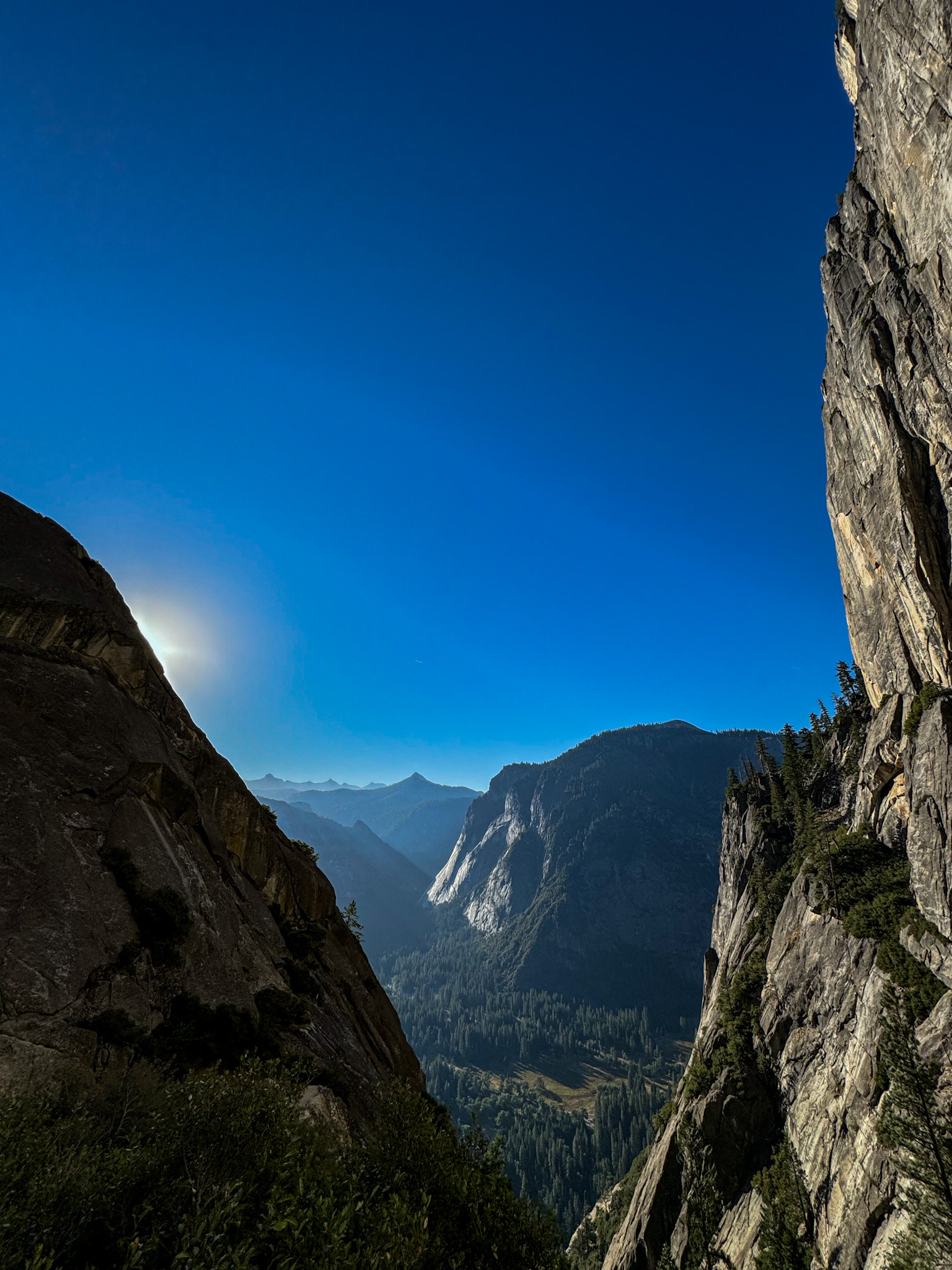 View of Yosemite Valley framed by steep granite cliffs with sunlight over the mountains.
