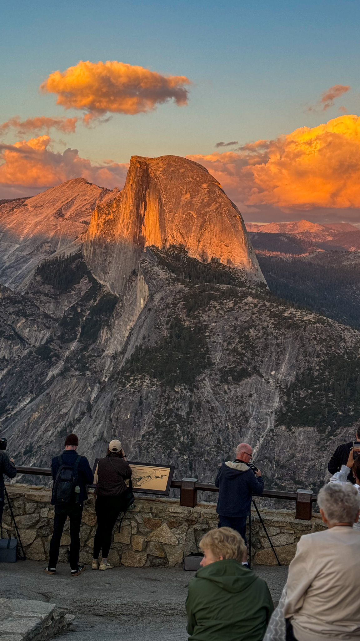 Half Dome glowing at sunset in Yosemite National Park with visitors viewing from Glacier Point overlook.