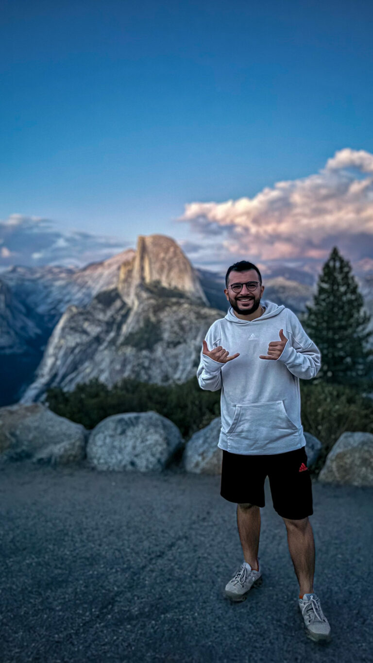 Person standing at Yosemite viewpoint with Half Dome in the background during sunset.