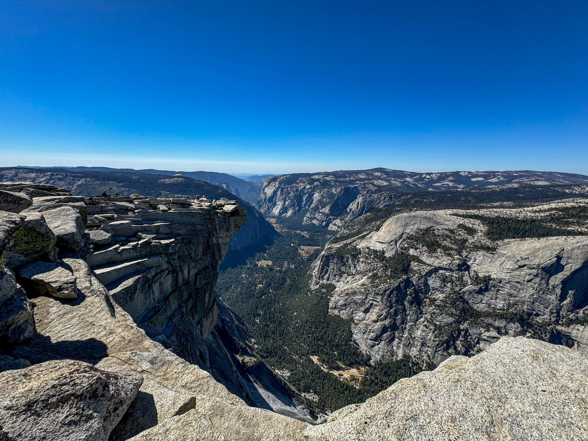 Panoramic view of Yosemite Valley from a high granite cliff with mountains and forest below.