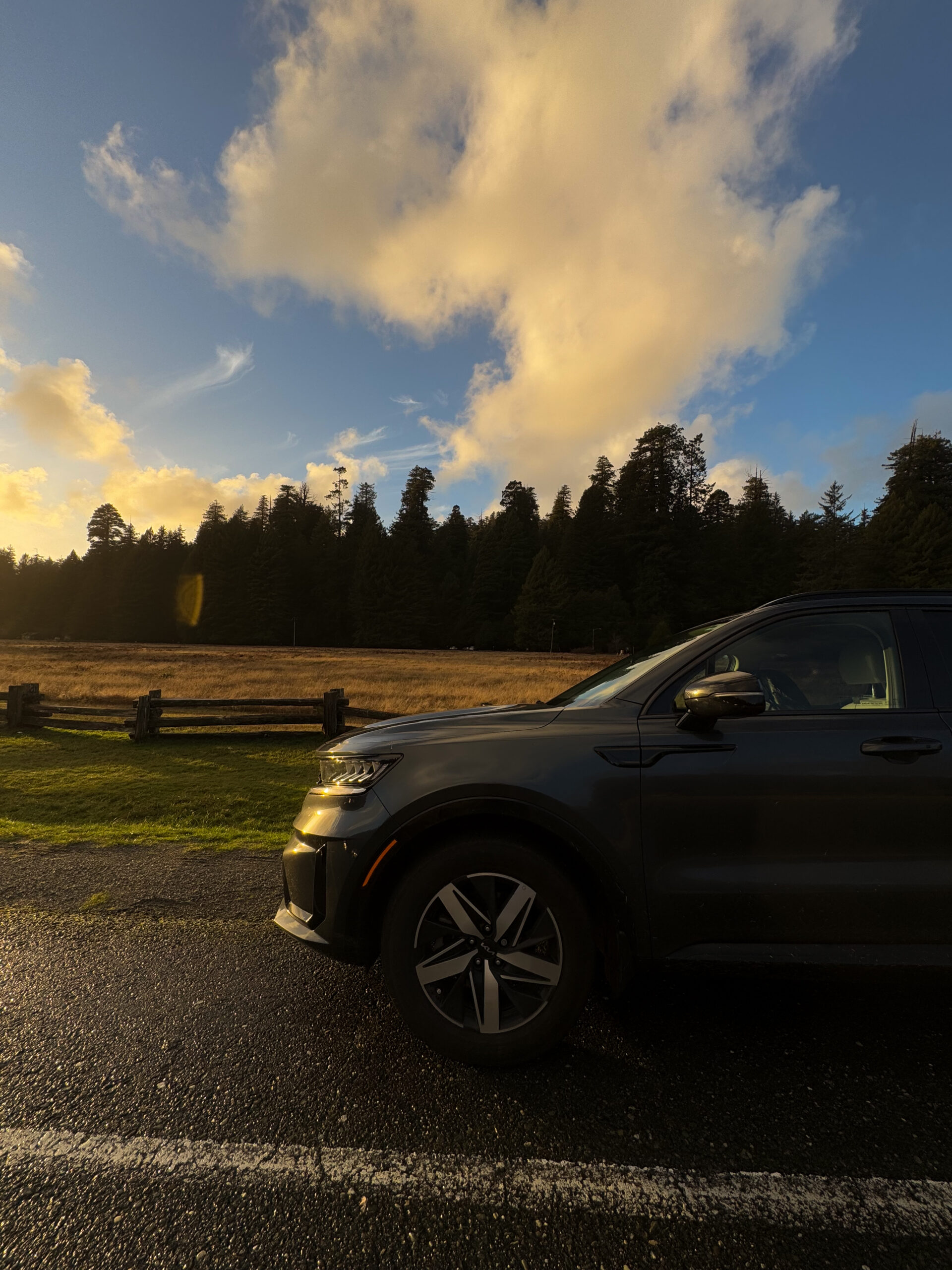 Car parked along a road near Redwood National and State Parks during sunset with forest in the background.
