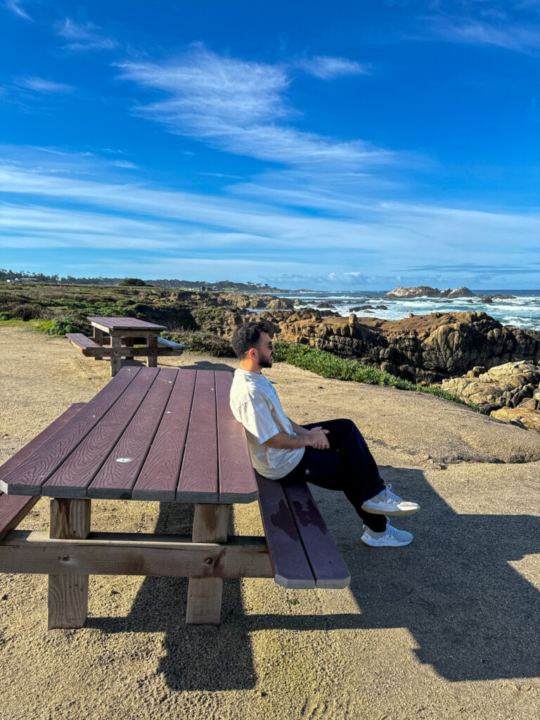 Traveler sitting near the rocky coastline along 17-Mile Drive in California.