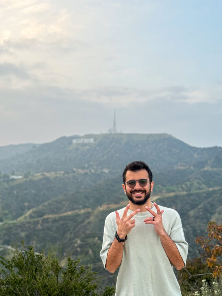 Traveler smiling with the Hollywood sign visible in the background hills of Los Angeles.