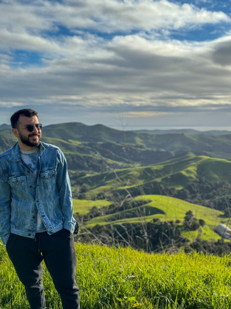 Traveler standing on a grassy hill overlooking rolling green California landscapes.