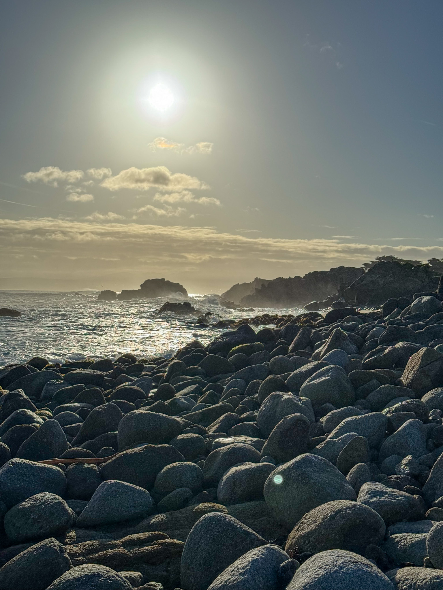 Rocky beach coastline with sunlight reflecting on the Pacific Ocean in California.