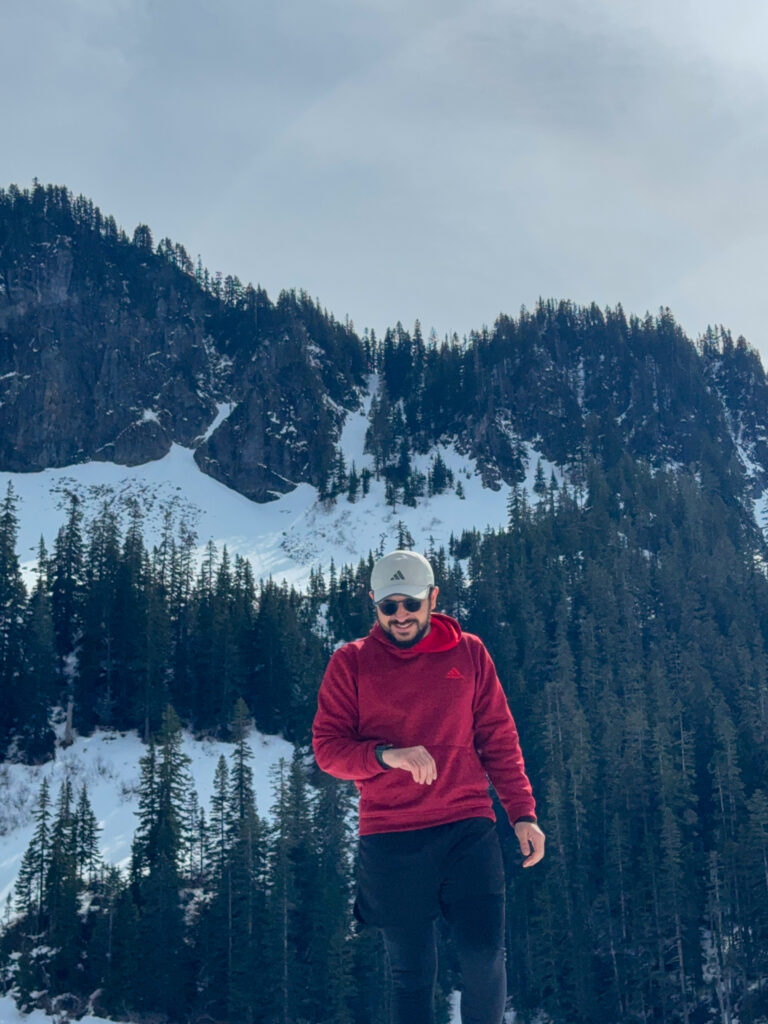 Hiker walking on snowy trail near Annette Lake with mountain backdrop in Washington.