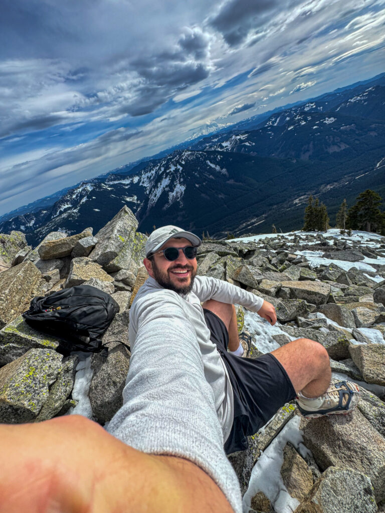 Hiker sitting on rocky summit of Granite Mountain with panoramic mountain views in Washington State.