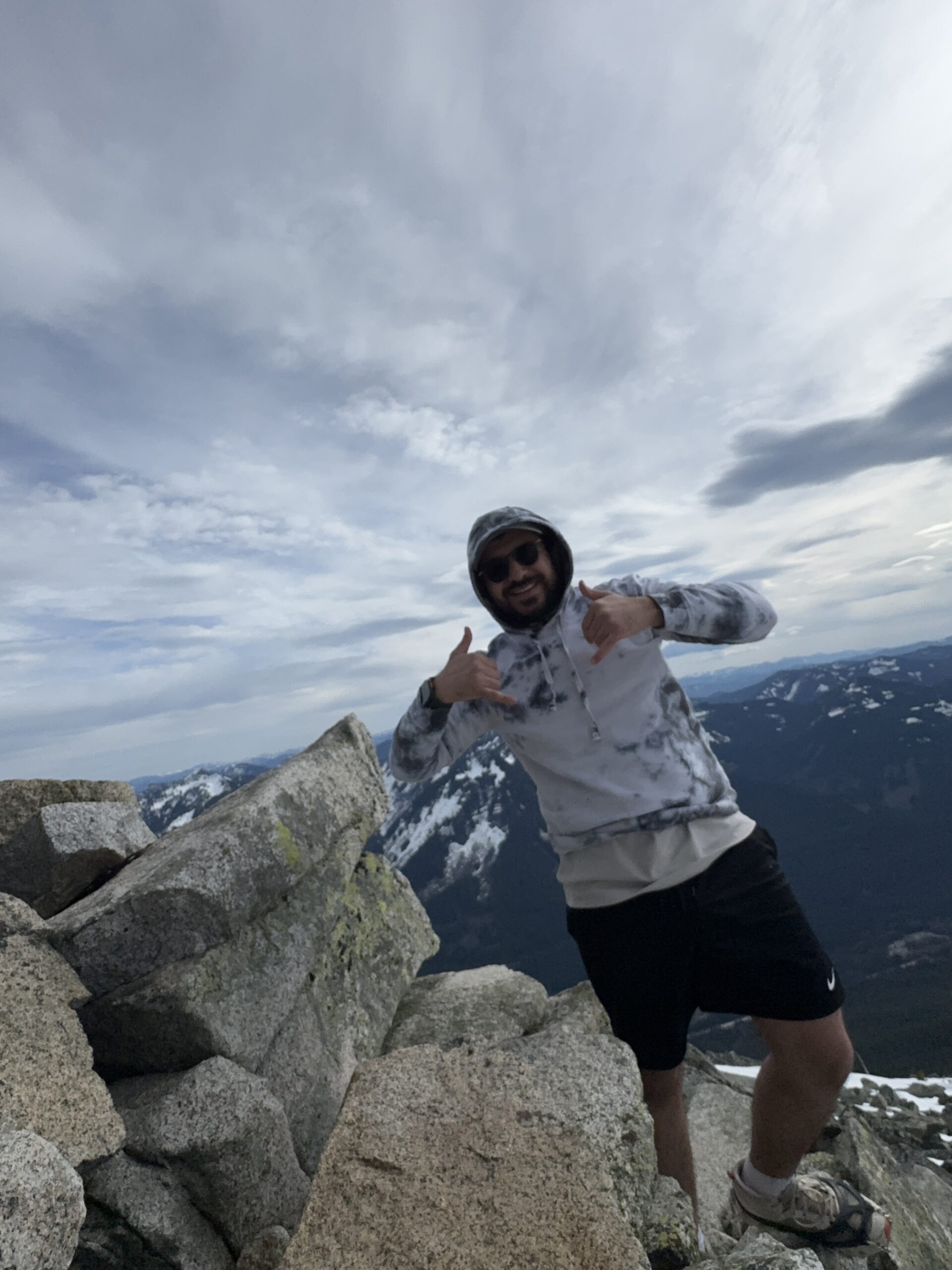 Hiker standing on rocky summit at Granite Mountain with panoramic mountain views and remaining snow in Washington.