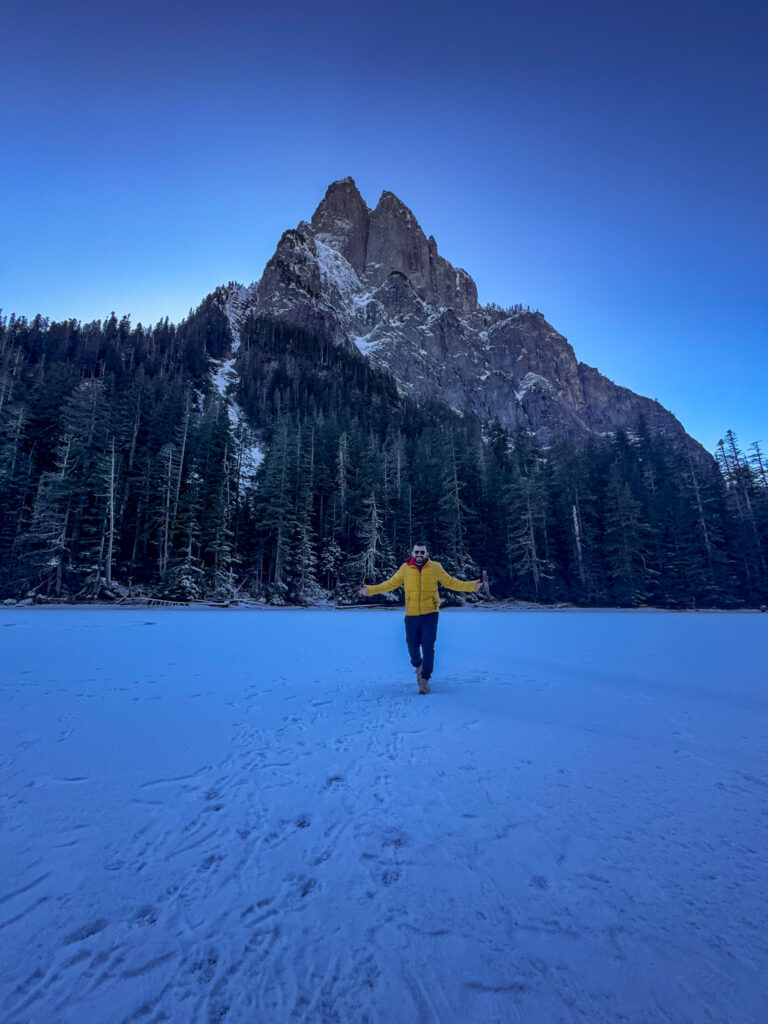Traveler standing on frozen Barclay Lake with snowy mountain scenery in Washington.