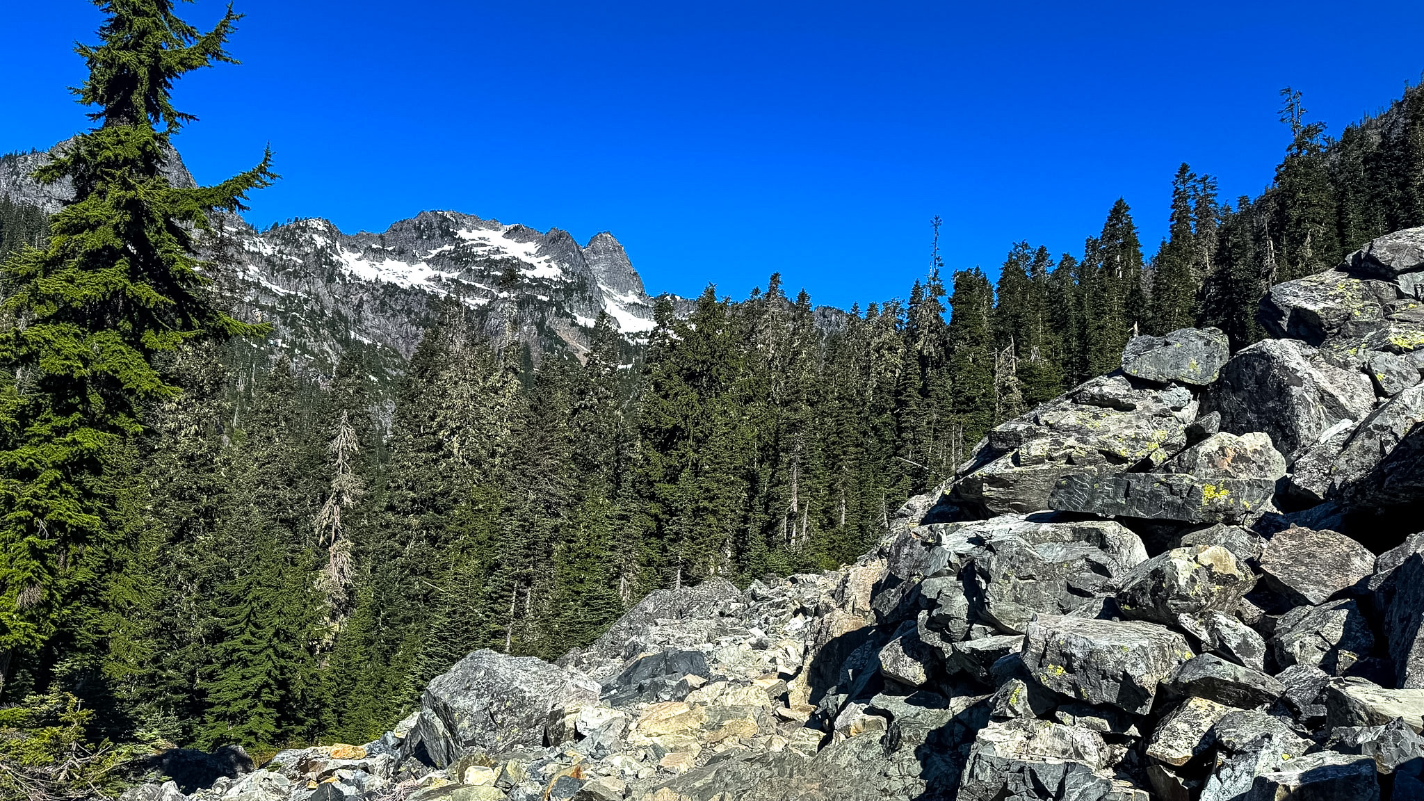 Large boulder field and alpine forest with rugged mountain peaks near Snow Lake in the Cascade Mountains of Washington.