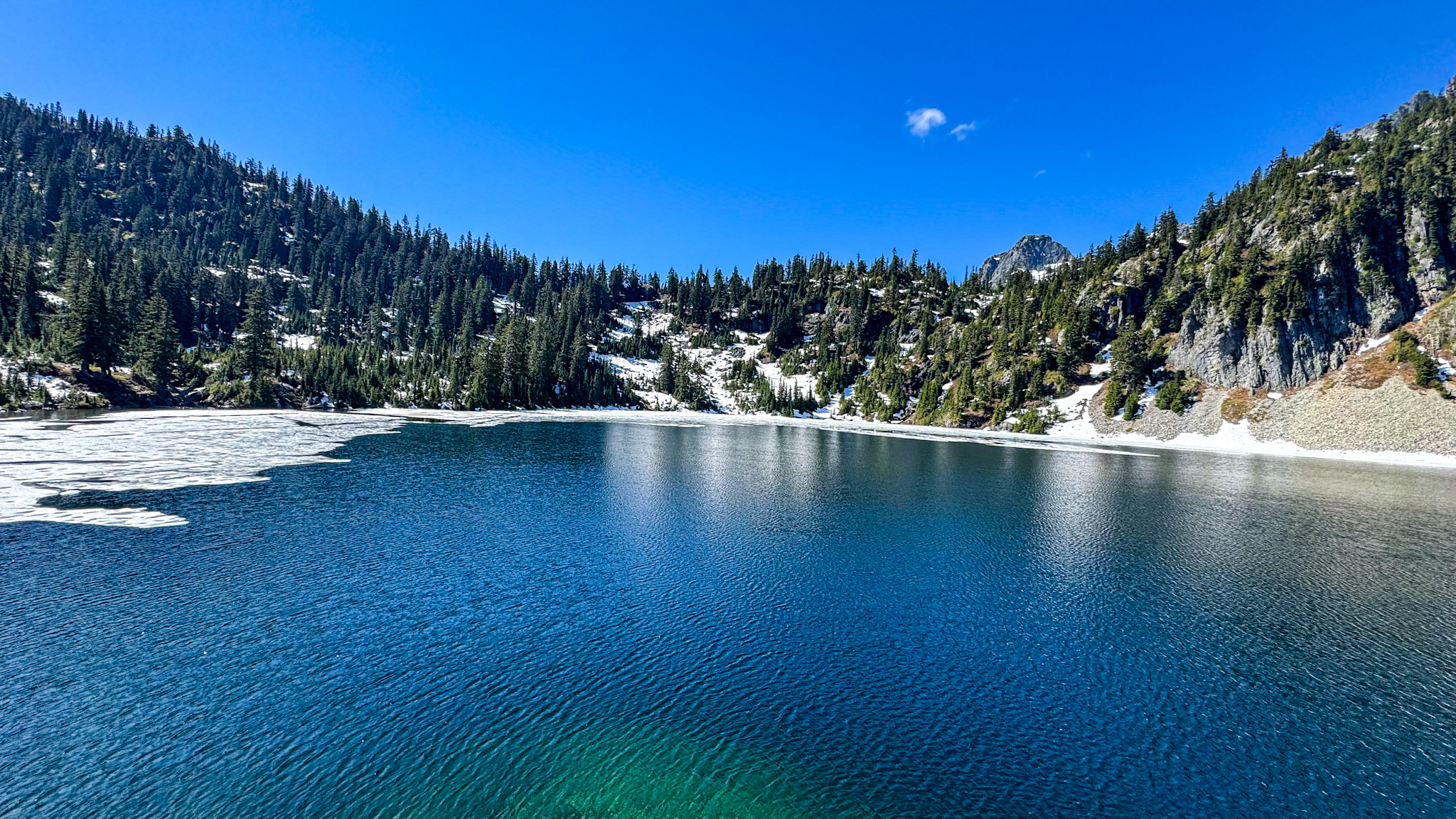 Snow Lake with clear blue water, lingering snow patches, and mountain scenery near Snoqualmie Pass, Washington.