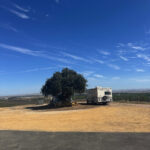 Wide view of a Harvest Hosts RV campsite overlooking vineyards and rolling farmland in California.