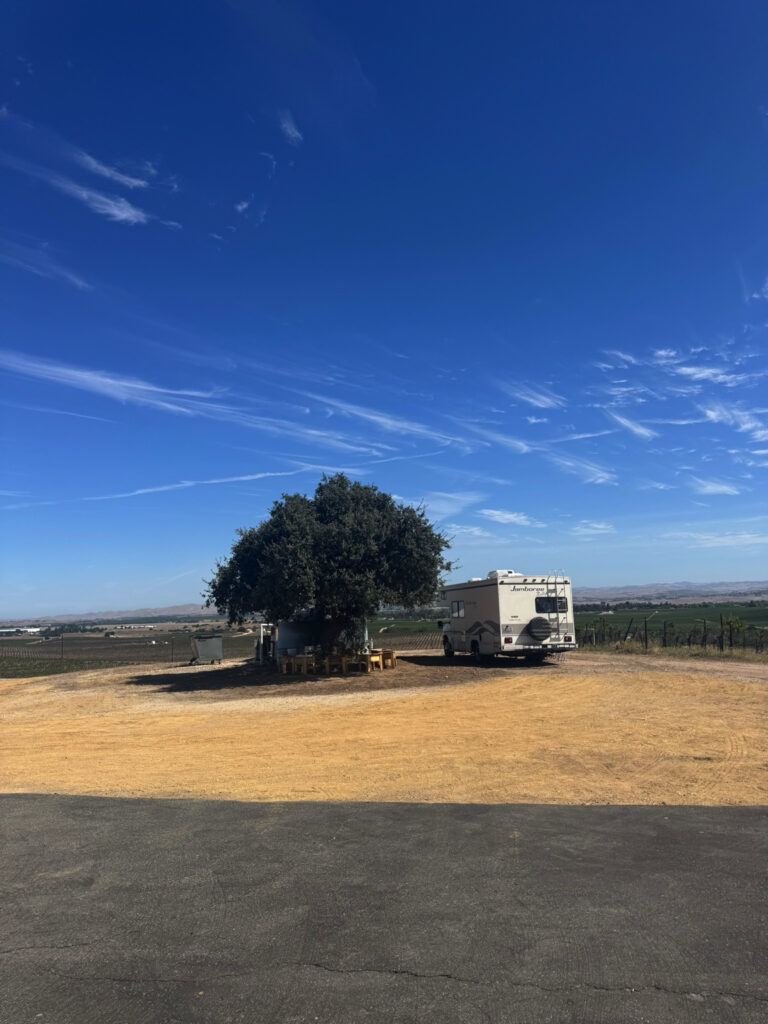 Wide view of a Harvest Hosts RV campsite overlooking vineyards and rolling farmland in California.