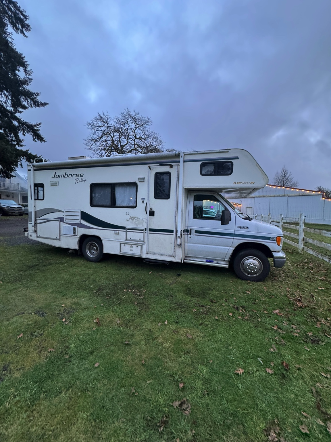 Class C RV parked overnight on a grassy campsite at a Harvest Hosts farm surrounded by white fencing and peaceful countryside.
