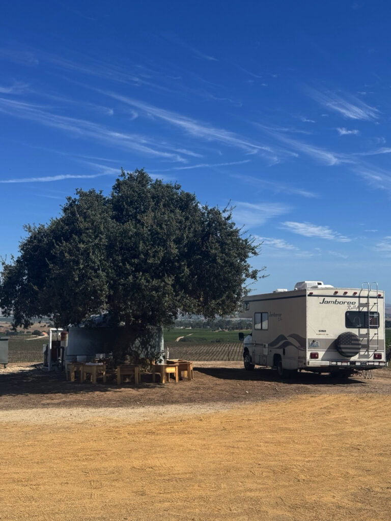 Class C RV parked overnight at a Harvest Hosts farm surrounded by vineyards and farmland in California.